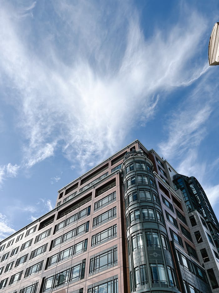 Low angle view of a modern office building under a bright blue sky with wispy clouds.