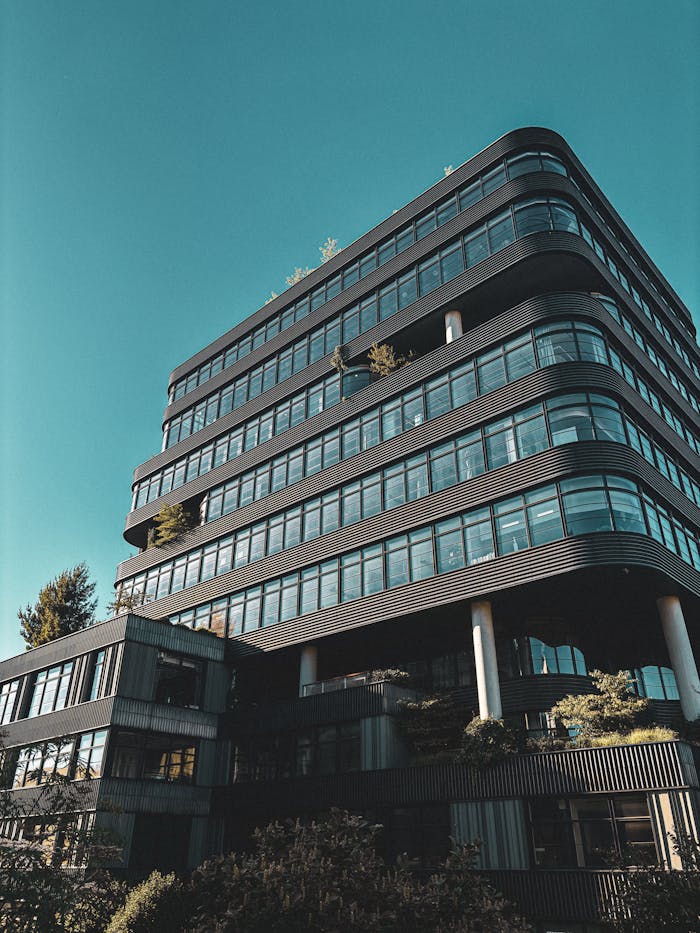 A modern office building with a curved glass facade against a clear blue sky in New York City.